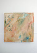 An abstract canvas painting with soft blended brushstrokes in peach, beige, cream, light blue, and touches of green, hanging on a plain white wall.